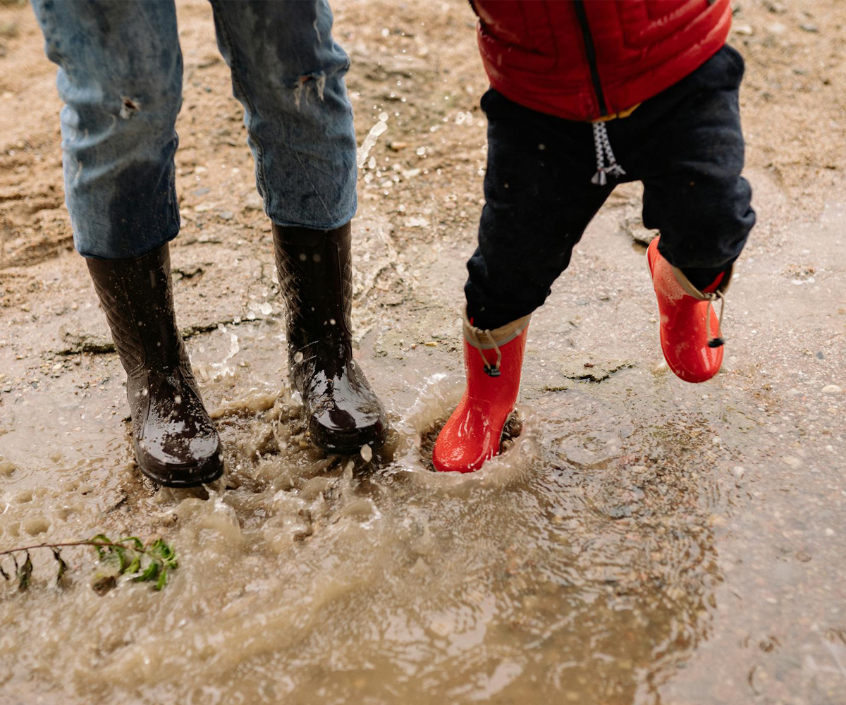 Two people wearing rain boots with their feet in a puddle.