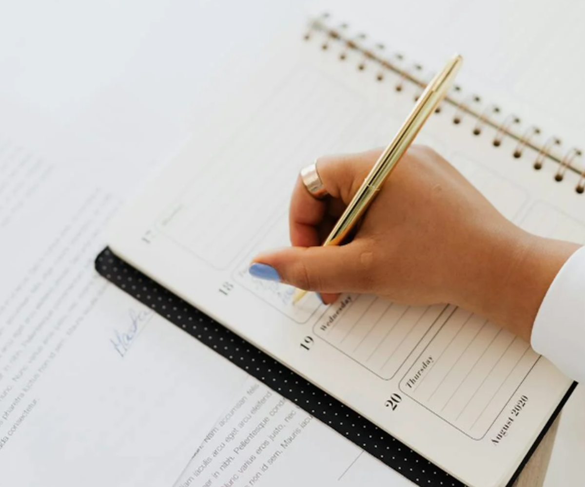 A person writing in a weekly agenda book.