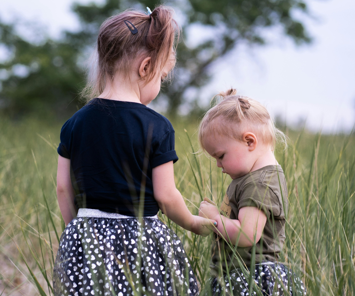 Two young girls standing together in the grass.