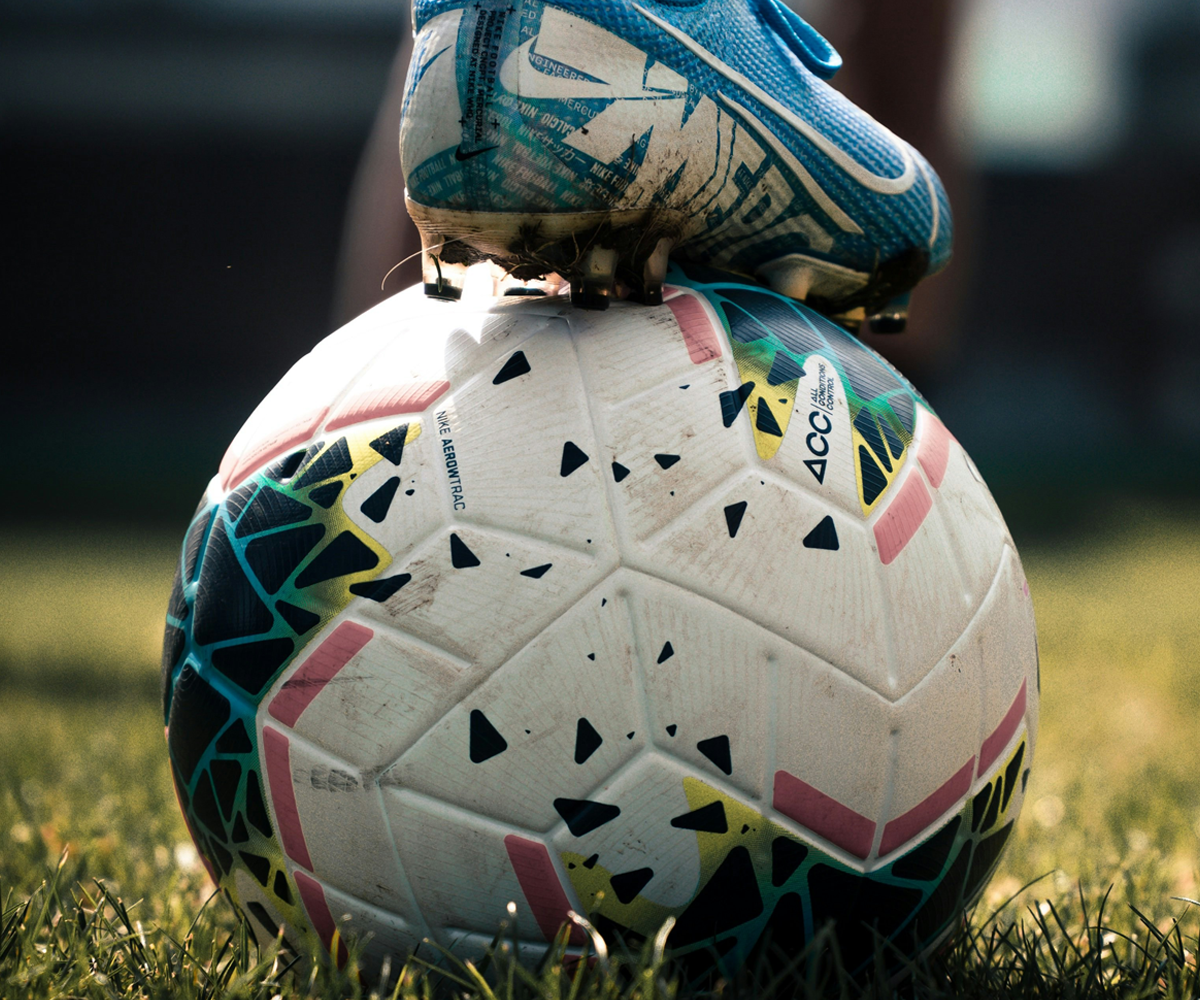 A person's foot in soccer cleats stepping on a soccer ball in the grass.