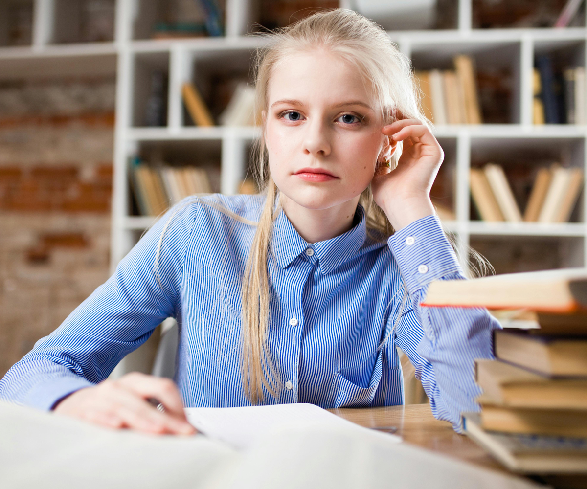 A young female student sittting at a desk with books in front of her.