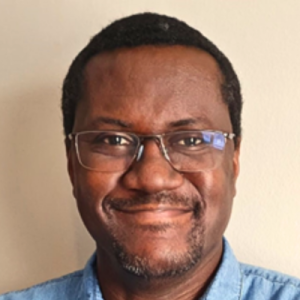 Portrait of a Barbadian man with black hair, a beard, and a dark skin tone, wearing glasses and a blue shirt.