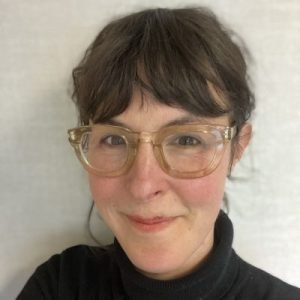 Portrait of a brown-haired woman of European descent, with a light skin tone, wearing glasses and black shirt.