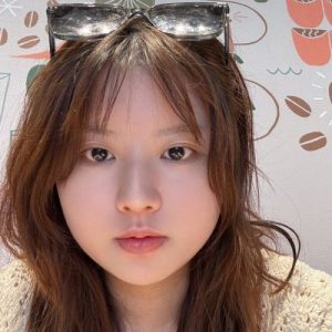 Portrait of a Chinese woman with brown hair and a light skin tone, wearing sunglasses and white shirt.