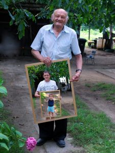 An older man is pictured here holding a photo of his son, who is also holding a photo of his son, depicting three generations.