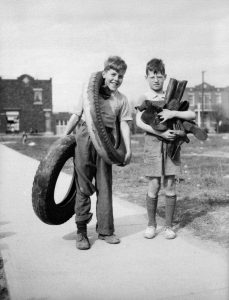 In this black and white photo, two young boys collect rubber (boots, shoes, and tires) during World War II.