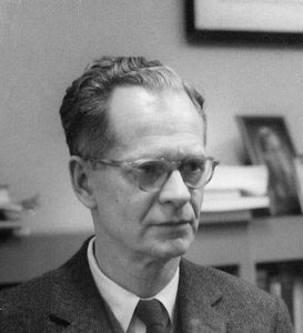 A black and white image of B.F. Skinner, a thin white man wearing glasses, staring stoically to the right of the camera