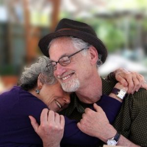 An older couple with grey hair shares an embrace.