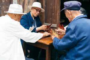 a small group of older Chinese men sit around a table playing a game