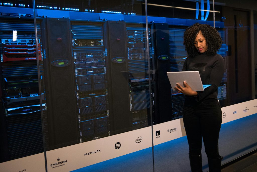 Women standing with laptop in hand beside server racks