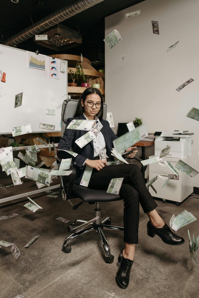 Women sitting in office chair with money flying all around her
