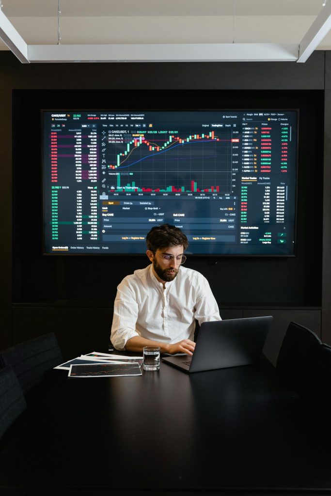 Man at table with big screen behind him showing data