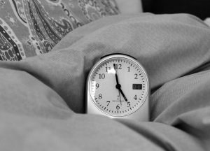 A clock that says 5 am sitting on a bed.