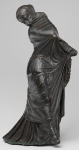 Bronze sculpture of a masked female dancer mid-motion, draped in a thin, flowing veil with arms raised and fabric extending behind her.