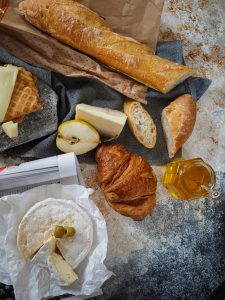 Baguette, croissant, fromage, poire, crackers et pot de miel disposés sur une table, illustrant un petit-déjeuner ou un goûter français.