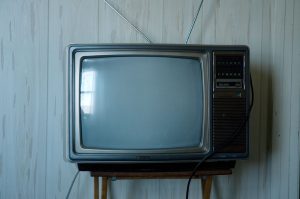 Télévision ancienne à écran cathodique avec antennes en métal, posée sur une petite table devant un mur en bois clair.