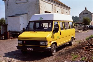 Minibus jaune Citroën C25 stationné sur une rue pavée devant un bâtiment en briques blanches.