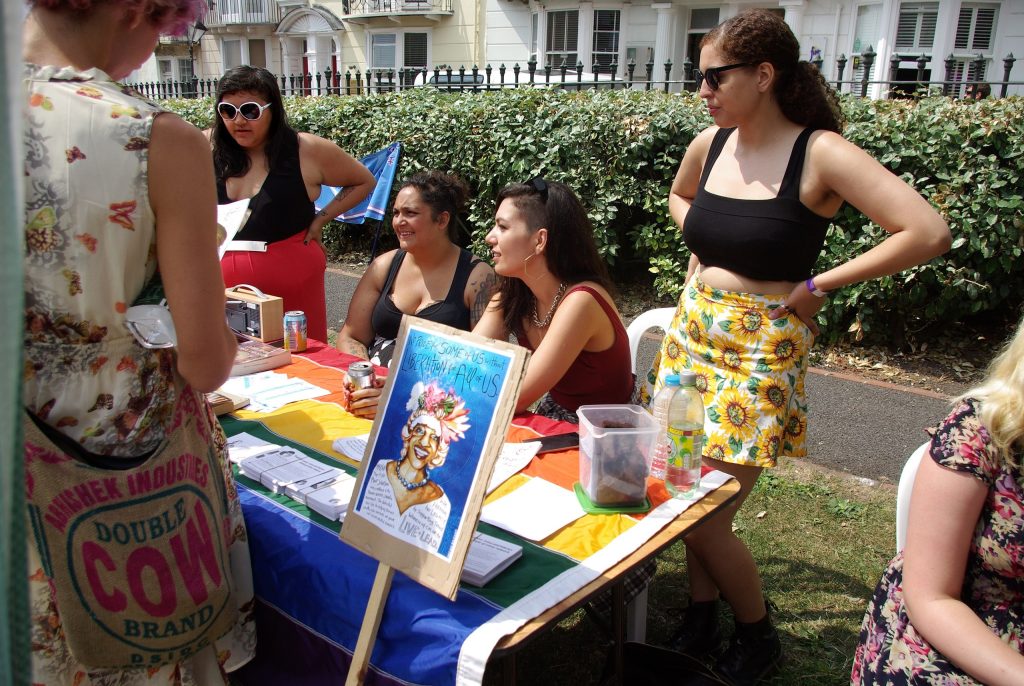Five people stand around a table in bright sunlight with flyers and a portrait of Marsha P. Johnson.