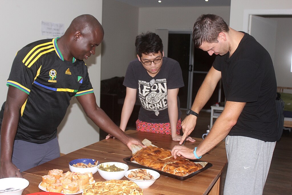 Three people cutting into a tart on a buffet table.
