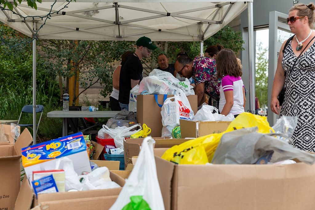 Under a tent, people look over cardboard boxes of food ready to give away.