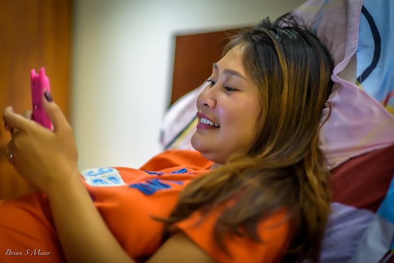 Smiling girl lying on pillows with pink smart phone