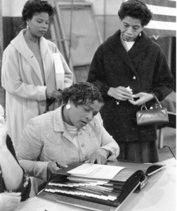 Three African American women at a polling place, one looking at a book of registered voters on November 5, 1957, in New York City or Newark, New Jersey