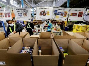 Open cardboard boxes at a food bank, workers in vests sort items.