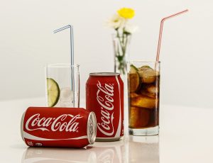 Two Coca-cola cans and two glasses with ice and straws on white table with white background