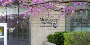 Exterior of the McMaster Health Sciences building with purple flowers blooming in a tree in front.