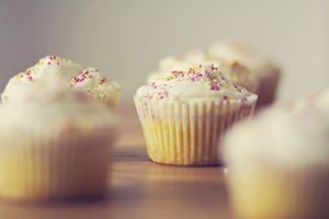 There are three vanilla cucakes in this photo. They have white icing and coloured sprinkles on top.