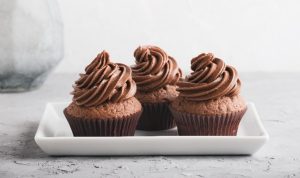 There are three chocolate cupcakes on a plate here. Each cupcake has a swirl of chocolate icing on top.