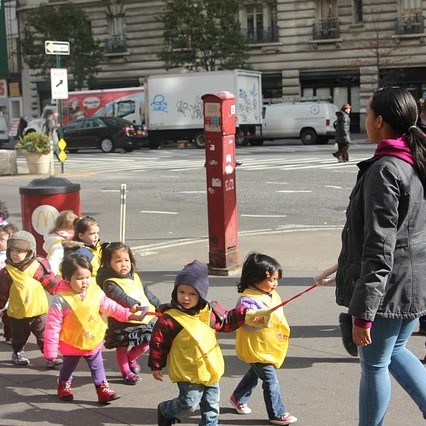 children holding rope wearing safety vests crossing street