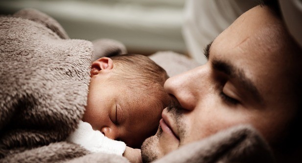 A male with an infant sleeping on his chest