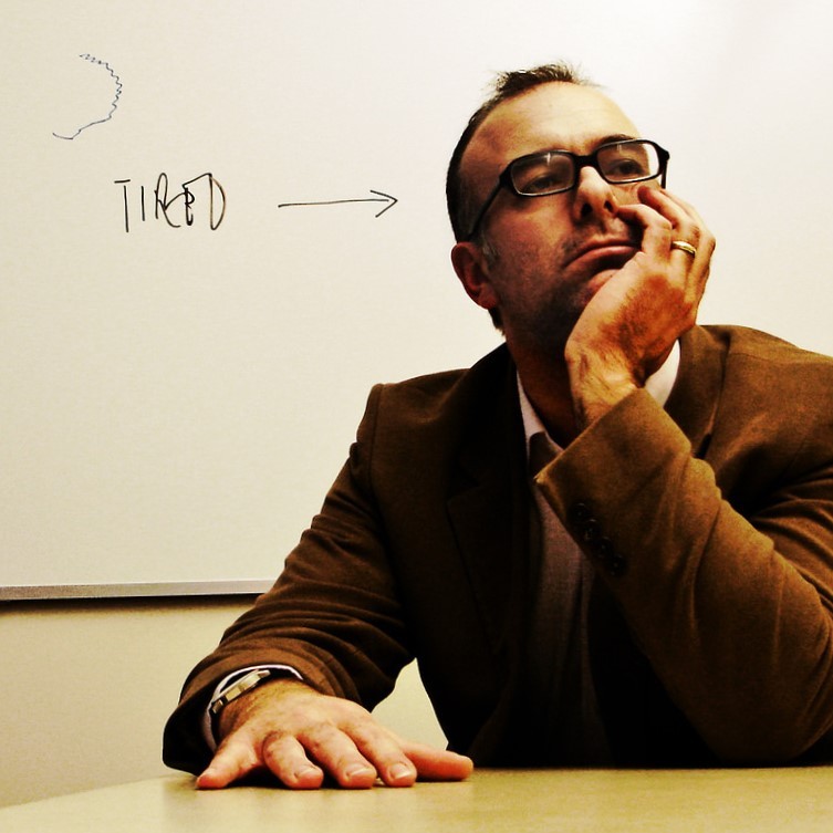 photo of a man with his head on his chin the word "tired" written beside him 