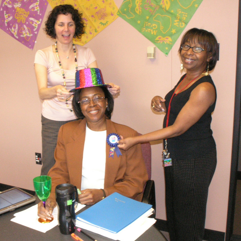 Photo of three people: one is sitting two are standing. They are all smiling