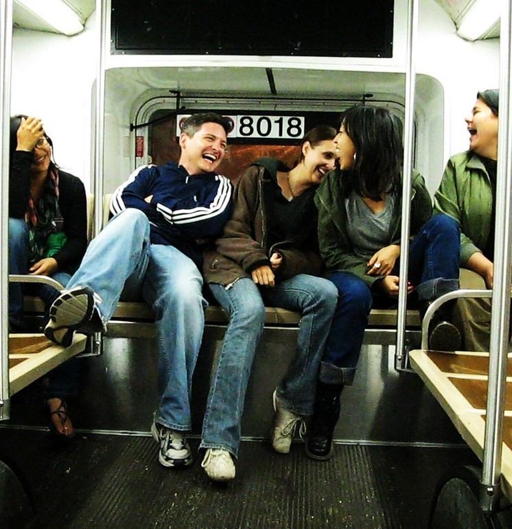 group of people sitting at the back of a subway car laughing