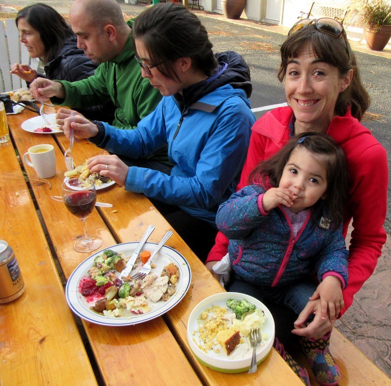 photo of people sitting at a picnic table eating outside.