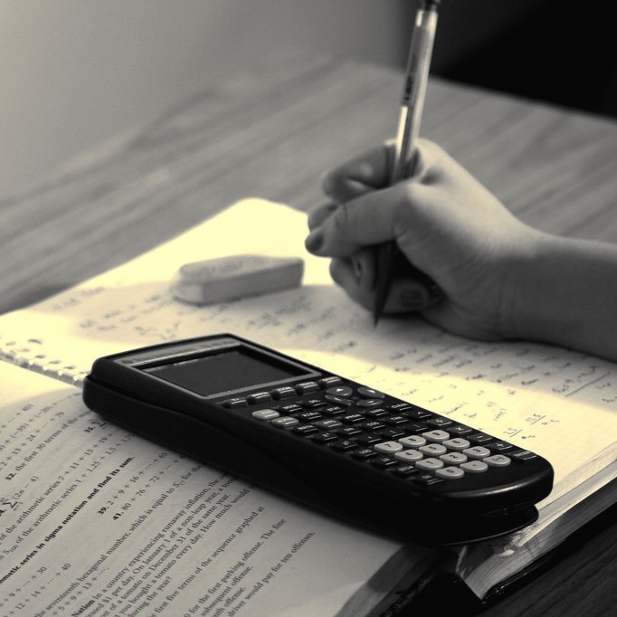 photo of a hand holding a pencil with an open book and a calculater