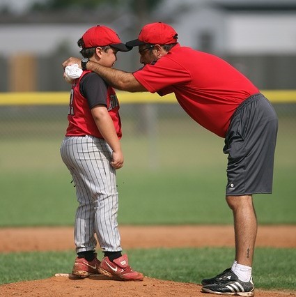 photo of a man speaking to a child dressed in a baseball uniform in a baseball field