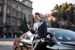 person leaning on car while checking cell phone messages