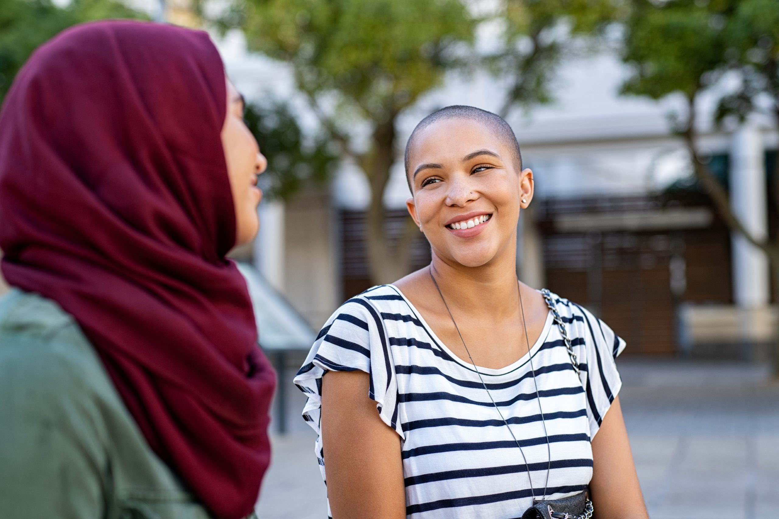 There are two multiethnic women, one of which is wearing a hijab talking with each other. This is a symbol for interviewing women and gathering research.