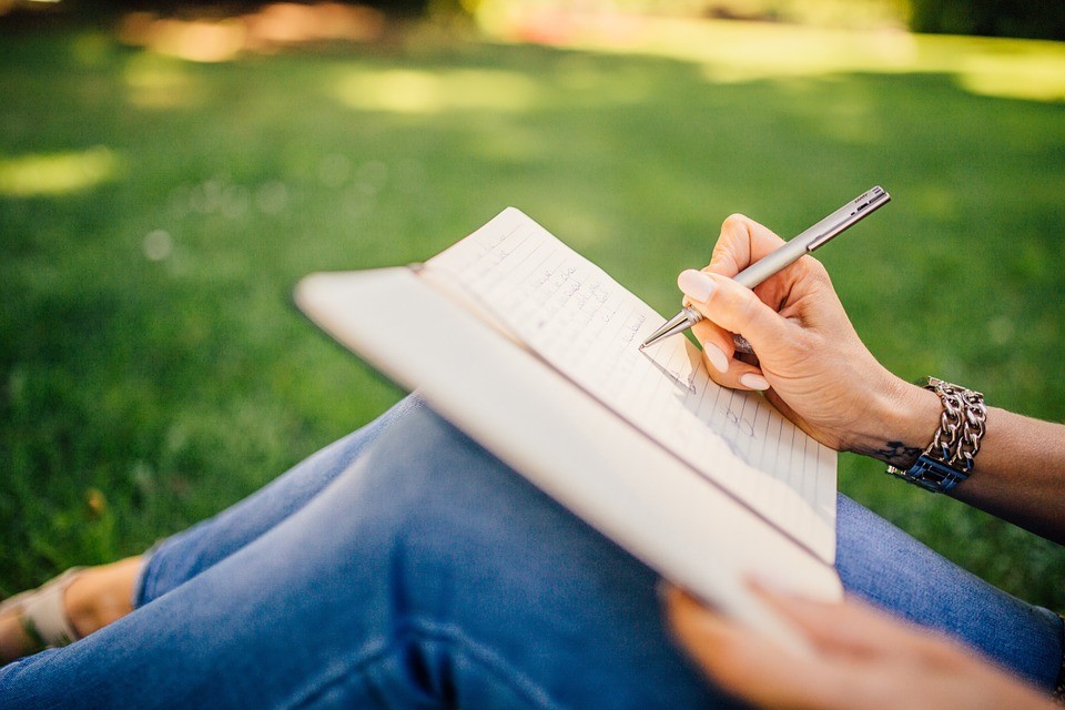 a woman writing down notes in a journal while seated in a field