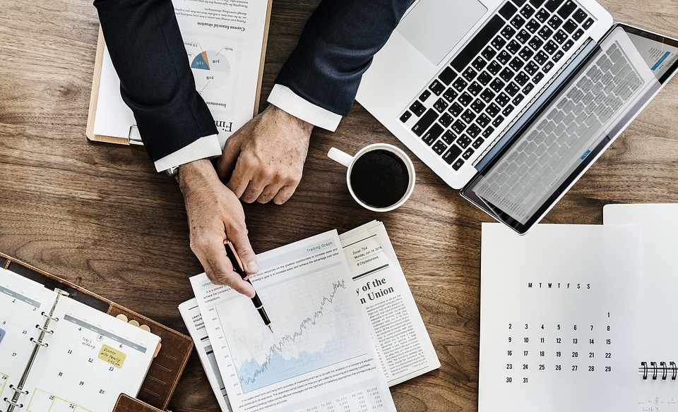 a person pointing to a graph among other papers and work items on a desk