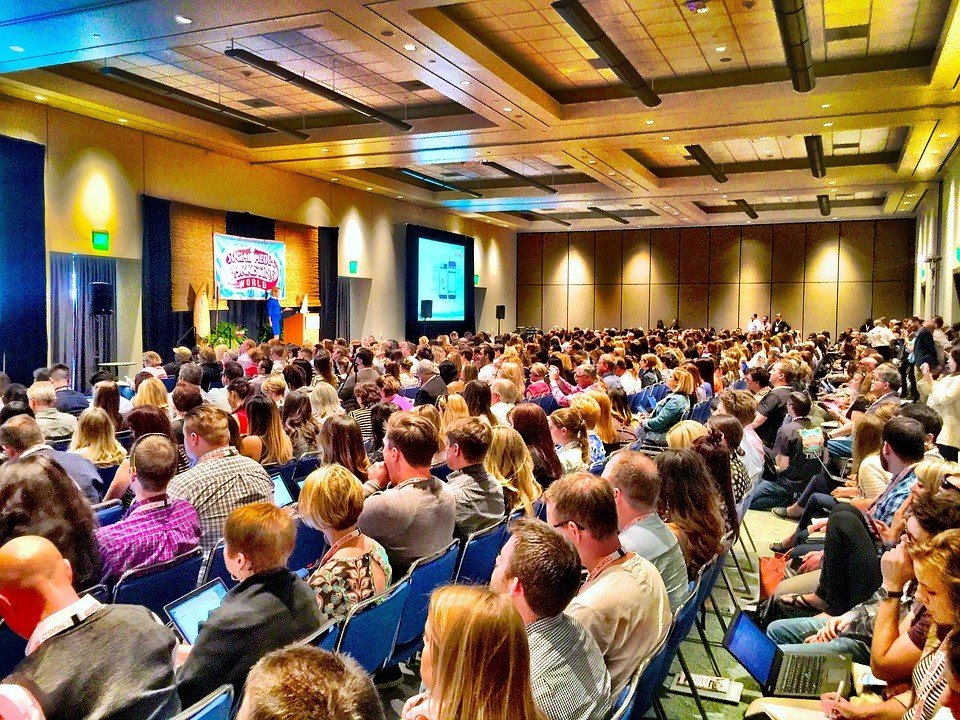 photo of many people in a large auditorium listening to a speaker