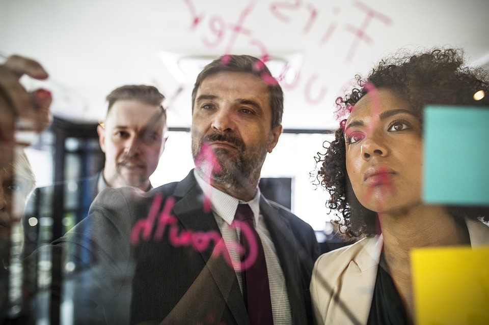 three people writing on a clear board with post-it notes, planning something