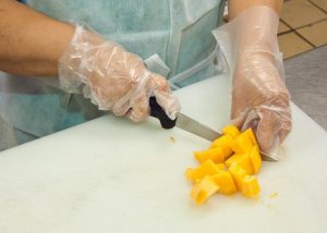 A person chops fruit while wearing gloves and gown
