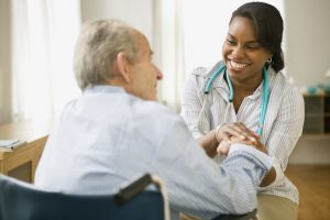 A woman clasps the hand of her client, who sits in a wheelchair.