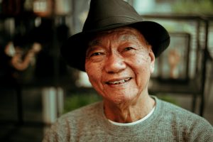 A smiling older man of Asian descent, wearing a fedora.