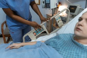Photo of a person pushing a button on a hospital bed with a patient in the bed.