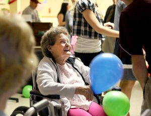 A senior woman smiles widely while holding two balloons.